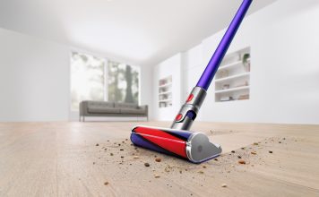 On voit l’aspirateur-balai sans fil V11 Absolute Pro en train de nettoyer un plancher en bois franc dans une salle blanche. Il passe à travers la poussière et les débris sur le plancher en ne laissant rien derrière.