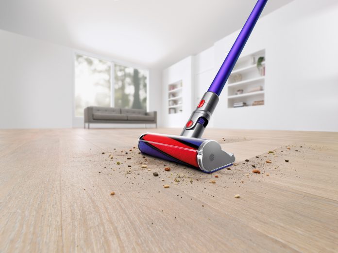 On voit l’aspirateur-balai sans fil V11 Absolute Pro en train de nettoyer un plancher en bois franc dans une salle blanche. Il passe à travers la poussière et les débris sur le plancher en ne laissant rien derrière.