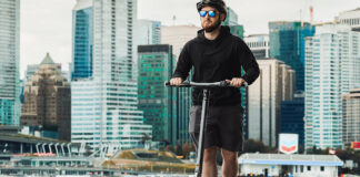 A man rising the Apollo City electric scooter by the water and smiling.