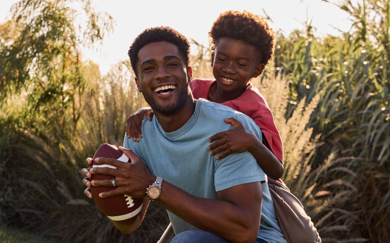 father and son playing baseball in a field. The dad is wearing a Citizen stylish watch.