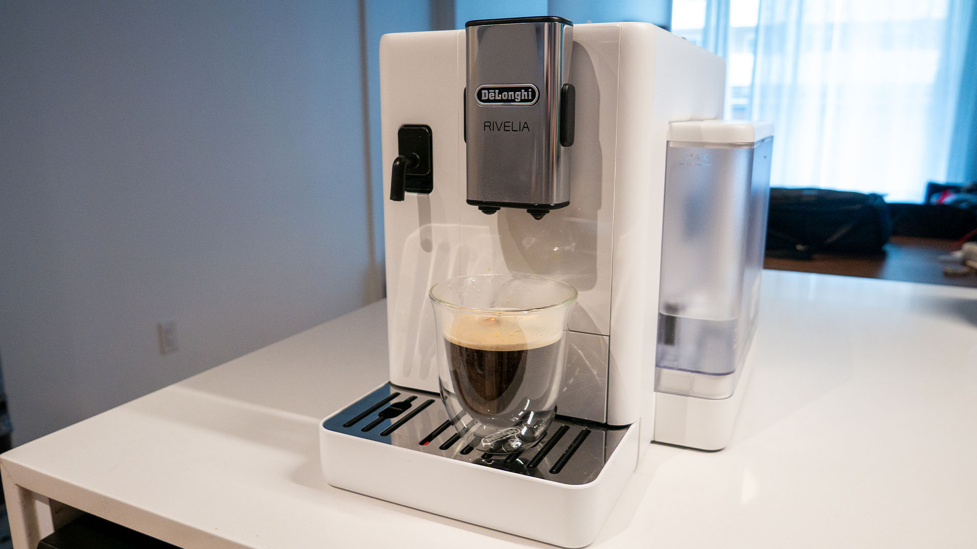 Image de la machine à espresso automatique Rivelia de De'Longhi sur un comptoir de cuisine avec une tasse à café