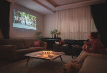 Woman watching home cinema projection - gifts for film lovers - with her dog in the living room at home.