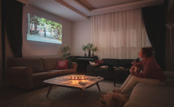 Woman watching home cinema projection - gifts for film lovers - with her dog in the living room at home.