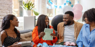 Smiling pregnant woman getting gifts for new parents at baby shower. Happy mother to be receiving presents from friends at baby shower party.