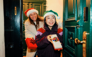 Girlfriends in festive hats arriving at the door, holding wrapped gifts and holiday drinks.