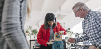 A woman receiving last-minute gifts in a bag from her colleagues and celebrating at the office after a recent success.