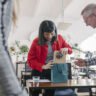 A woman receiving last-minute gifts in a bag from her colleagues and celebrating at the office after a recent success.