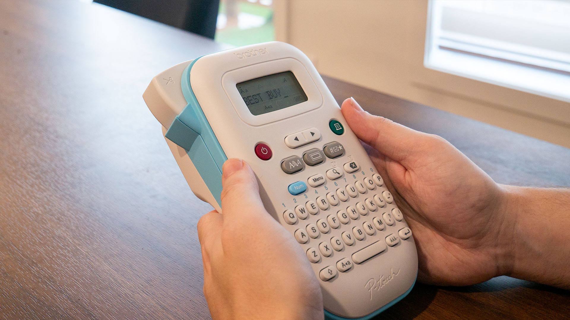 Image de la Brother P-touch PT-N10 dans les mains d'une personne posée sur une table
